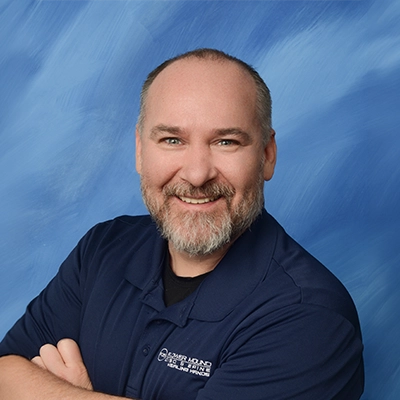 Chiropractor Kevin Pederson Smiling In Front Of Blue Background