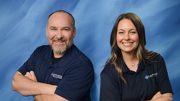 Chiropractors Kevin Pederson & Brittany Pando Smiling In Front Of Blue Background